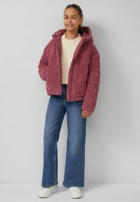 Roze corduroy pufferjack met capuchon, textuurstof en ribbelontwerp, gedragen over een lichte trui en gecombineerd met blauwe flared jeans.