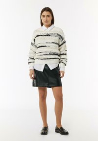 Un pull blanc duveteux avec des rayures noires, superposé à une chemise blanche à col et accompagné d'une jupe en cuir noir et de mocassins noirs.