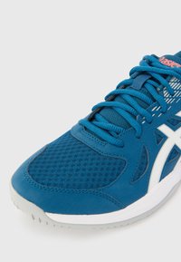 Chaussure de sport bleue avec une tige en mesh, accents blancs, design texturé et lacets plats. La semelle est gris clair avec un motif de semelle.