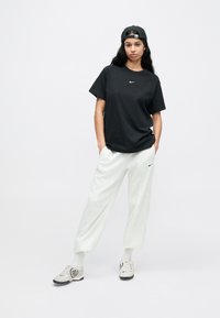 Juoda trumpomis rankovėmis marškinėliai su balta logotipu, pilkos sportinės kelnės ir pilkos sportbačiai su logotipu. Kepurė dėvima atbulai. Paprastas, kasdieniškas sportiškas aprangos stilius.