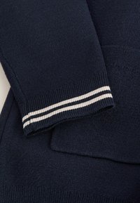 Marineblauwe trui met geribde manchetten en witte strepen. Zachte gebreide textuur, met een ronde hals en een rechte snit.