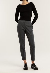 Czarny prążkowany top z długim rękawem w połączeniu z dopasowanymi szarymi spodniami z przodu z zakładkami. Czarne sznurowane buty dopełniają stylizację.