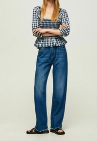 Blusa a quadri leggera e aderente con orlo a peplum e maniche a tre quarti, abbinata a jeans blu larghi e strappati e sandali bassi.