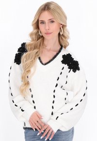 Weißer Strickpullover mit schwarzen Blumenakzenten an den Schultern, V-Ausschnitt-Design und strukturierten, lockeren Ärmeln mit schwarzem Stich.
