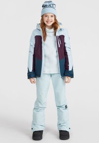 Veste d'hiver bleu clair avec des accents marine et bordeaux, associée à un pull en laine bouclée bleu clair et à un pantalon de ski. Des bottes de neige noires complètent la tenue.
