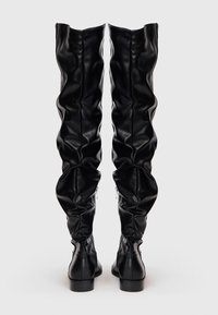 Botas de cuero negro por encima de la rodilla con un diseño arrugado, punta redonda y un tacón bajo tipo bloque, con cremalleras en los lados exteriores.