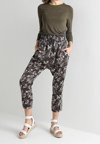Donker bloemenpatroon broeken met elastische tailleband, cropped ontwerp en zijstrepen. Gecombineerd met een getailleerd olijfgroen topje en witte sandalen.
