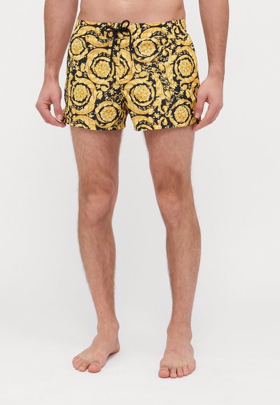 Bañador negro con un patrón amarillo ornamental, que cuenta con una cintura con cordón y un ajuste cómodo. El material parece ligero y suave.