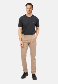 T-shirt nera a girocollo con logo dorato, abbinata a chinos color sabbia e sneakers nere, caratterizzata da una vestibilità rilassata e una texture di tessuto liscia.