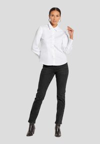 Weißes Hemd mit langen Ärmeln, Kragen und taillierter Passform. Kombiniert mit schwarzen Jeans und Stiefeletten, was einen modernen Look ergibt.