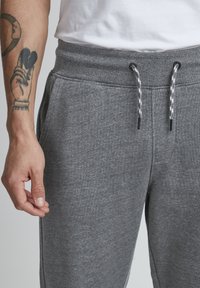 Gray jogger pants with a drawstring waist, side pockets, and a soft, textured fabric. Features contrasting black and white drawstring.