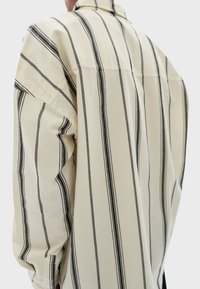 Camisa de manga larga en algodón beige, con rayas verticales negras. Corte relajado con un cuello estándar y puños de manga abotonados.