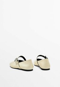 Beige læderballerinaer med åben hæl, der har en sølv spænde detalje og en lav sort sål. Glat tekstur med et minimalistisk design.