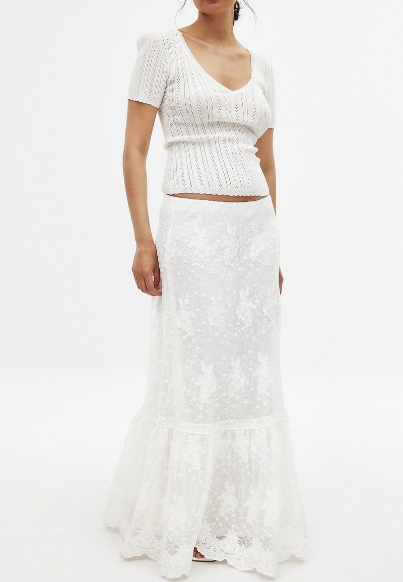 Top tricoté blanc à manches courtes et décolleté en V. Jupe blanche fluide avec superposition en dentelle, ourlet volanté et motif floral.