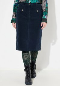 Námořnická kordová midi sukně s předními kapsami a zlatým kováním, v kombinaci se zelenými punčochami s krajkovým vzorem a černými šněrovacími botami.