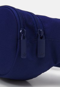 Marinblå tygpåse med dubbla dragkedjor, med texturerat material och små märkta dragkedjor. Kompakt design.