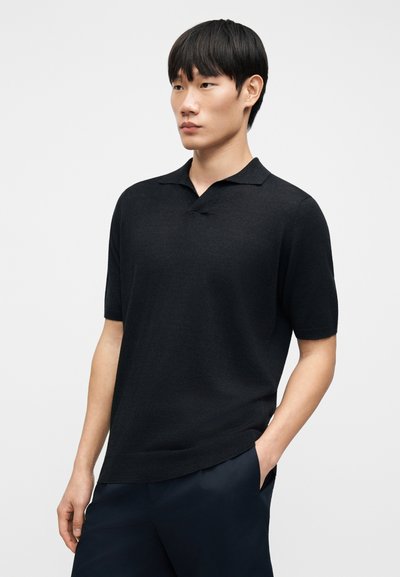 Polo noir à manches courtes en tissu doux avec un col classique. Présente une coupe décontractée et un design minimaliste.