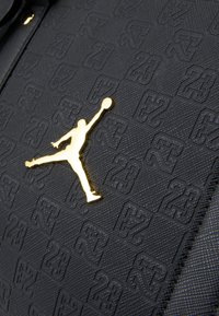 Material preto texturizado apresentando um padrão em relevo do número "23" e um logótipo Jumpman dourado exibido em destaque no centro.