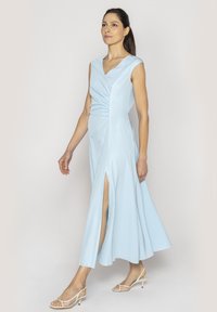 Jasnoniebieska sukienka bez rękawów z dekoltem w serek, rozcięciem po boku i marszczeniem w talii. Gładki materiał i zwiewna sylwetka w kształcie litery A.