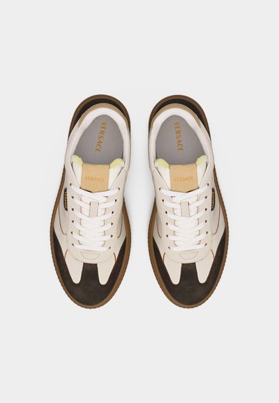 Paire de baskets Versace blanches et marron avec lacets, logo de la marque sur la languette et les côtés, et semelles couleur gomme, vue de dessus.