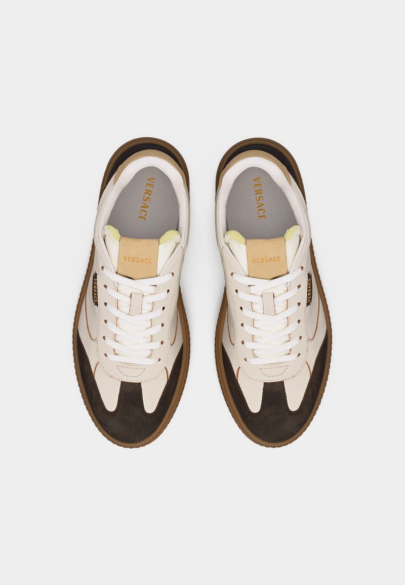 Coppia di sneakers Versace bianche e marroni con lacci, logo del marchio sulla linguetta e sui lati, e suole color gomma, viste dall'alto.