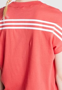 Camisa de color coral de manga corta con cuello redondo, que presenta tres rayas blancas horizontales en los hombros y una tela suave y texturizada.