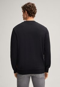 Felpa nera con maniche lunghe, collo e orlo a coste, materiale in cotone, texture liscia e piccolo logo dettagliato nella parte inferiore.