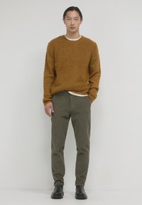 Rustfarbenes strukturiertes Sweatshirt mit Rundhalsausschnitt, kombiniert mit olivgrünen Cordhosen und schwarzen Stiefeletten.