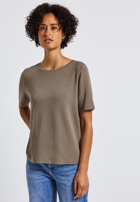 Khaki tričko s krátkým rukávem vyrobené z měkké tkaniny s kulatým výstřihem. V kombinaci s modrými džíny, které mají klasický střih a jednoduchý design.