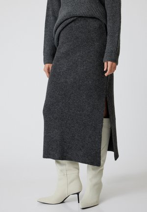 Charcoal gray knit skirt with side slit, paired with cream high-heel boots. Features a fitted waistband and soft, textured fabric.