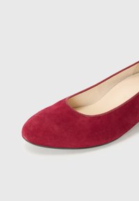 Røde suede ballettsko med avrundet tå og lavt snitt, med en myk innersåle og en solid svart yttersåle.