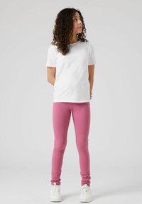 T-shirt en coton blanc associé à un legging rose. Les leggings ont une texture lisse, se rétrécissant vers la cheville, et sont portés avec des baskets blanches.