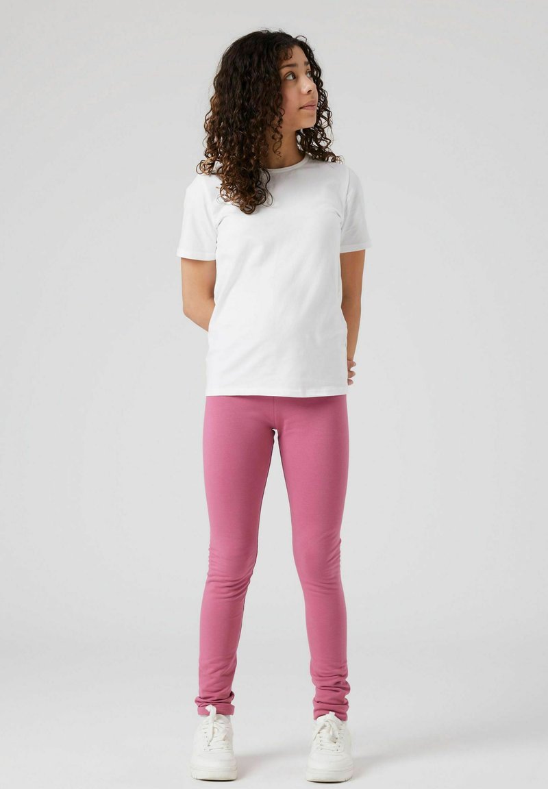 T-shirt en coton blanc associé à un legging rose. Les leggings ont une texture lisse, se rétrécissant vers la cheville, et sont portés avec des baskets blanches.