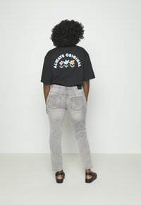 Camiseta preta com "ALWAYS ORIGINAL" e designs florais nas costas, combinada com jeans cinzas e sandálias pretas, exibindo um visual descontraído.