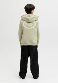 Felpa verde chiaro con cappuccio, caratterizzata da testo stampato bianco sul retro. Indossata con pantaloni neri in velluto a coste larghi.
