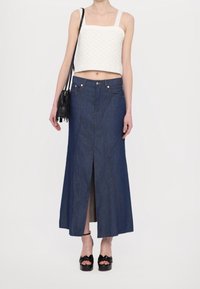 Denim lange rok met een vooruitsnijding, blauwe kleur, met contrasterende stiksels, gecombineerd met een witte geweven crop top en een zwarte crossbody tas.