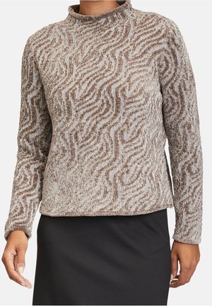 Femme portant un pull à manches longues à motif texturé beige et marron avec un col montant, associée à une jupe noire.