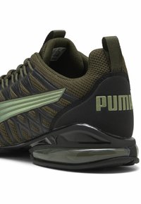 Zapatillas Puma con una parte superior de malla verde oliva y detalles en negro, patrón texturizado y un prominente talón de goma para soporte.
