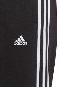 Pantalones deportivos negros con rayas laterales blancas y un logo de Adidas en blanco. Hechos de una tela suave y elástica con un diseño de ajuste estándar.