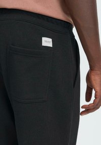 Zwarte joggingbroek van gestructureerde stof, met een achterzak met een klein label en een elastische tailleband.