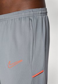 Gray athletic shorts made of lightweight fabric, featuring contrasting orange Nike logo and accent detail, with elastic waistband and side pockets.