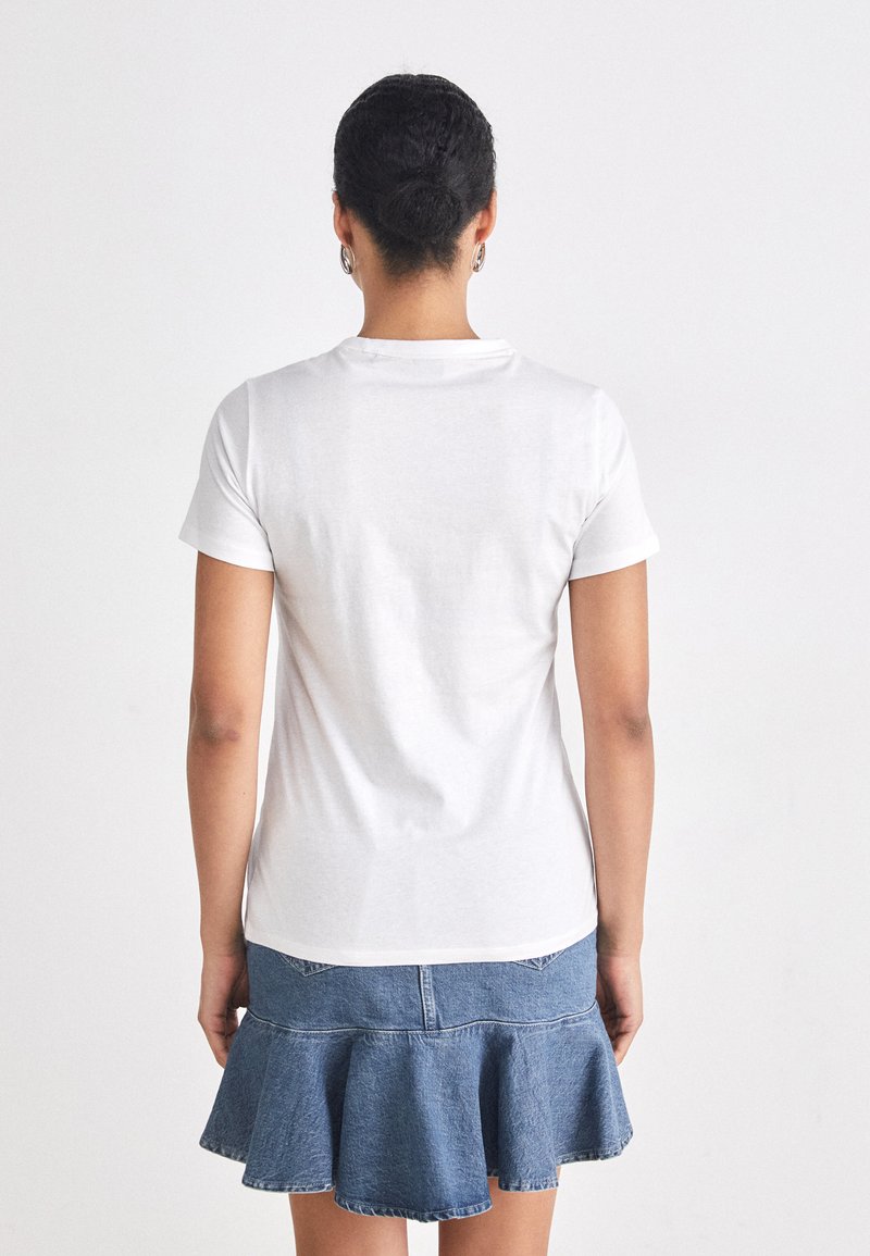 T-shirt en coton blanc à manches courtes, au design ajusté. Associé à une mini-jupe en denim avec un ourlet évasé et froncé, dotée de poches arrière.