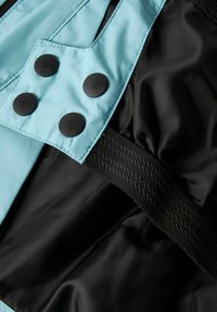 Blå nylonstof med sorte knapper og detaljer, der har en tekstureret sort strop og en glat indvendig foring. Designet inkluderer en lomme.