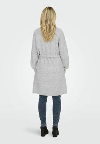Cardigan tricoté gris clair avec une taille ceinturée, des manches longues et une finition texturée; associé à un jean bleu foncé et des bottes à talons noires.