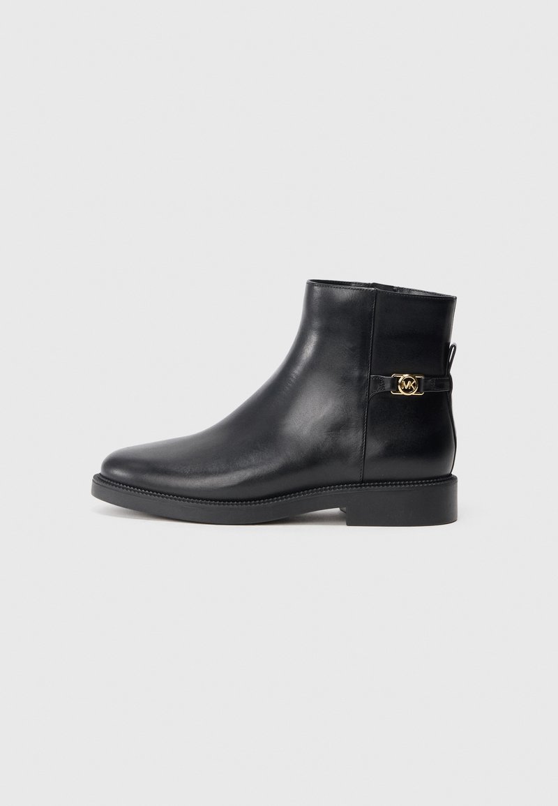 Bota de tornozelo em couro preto com bico arredondado, sola plana e detalhe em metal dourado numa faixa lateral. Textura suave, design minimalista.