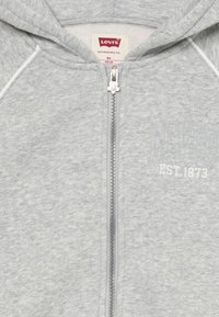 Graue Zip-Hoodie aus weichem Stoff, mit weißem Kordelzug und geprägtem Text "LEVI'S EST. 1873" auf der Vorderseite. Der Reißverschluss hat einen Blumen-Zipper.