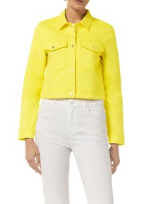 Cropped yellow denim jacket with two front pockets, silver hardware, and a classic collar, paired with white jeans. Smooth texture.