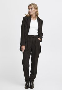 Zwart gestreept pak met een op maat gemaakte blazer en losvallende broek, gecombineerd met een witte top en zwarte enkellaarzen.