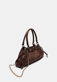 Sac à main en daim marron avec doubles poignées, quincaillerie dorée et une bandoulière en chaîne amovible. Présente des accents de œillets et une fermeture à cordon ajustable.