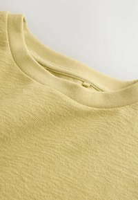 Világos sárga rövid ujjú póló texturált felülettel, bordázott kerek nyakkivágással és sima varrással a szélein.